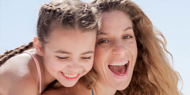 Two smiling girls at the beach, embracing each other happily.