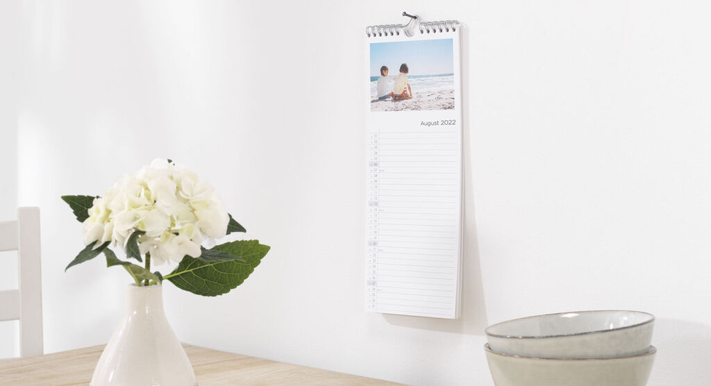 A wall calendar with a beautiful family photo and a blooming flower vase on a wooden table