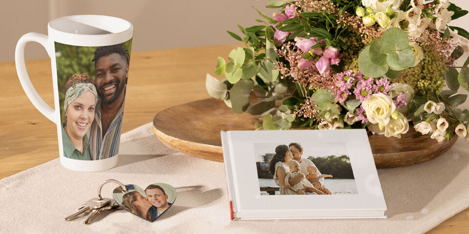 A lovingly decorated table with a cup, a photo book, and a heart-shaped keychain next to a bouquet.