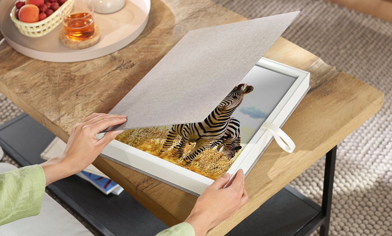 A person opens a picture frame with a zebra motif. The frame is bright, and the image shows a beautiful landscape.