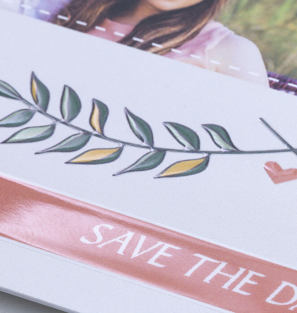 Close-up of a decorative branch with green and yellow leaves and the inscription "SAVE THE DATE" on an invitation.