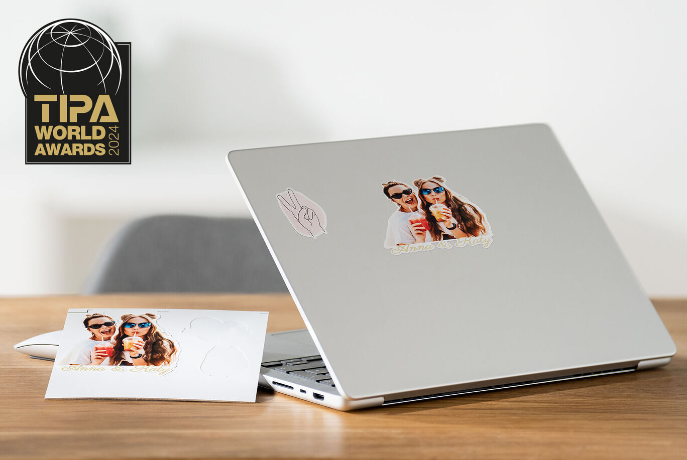 A laptop with a photo sticker of a couple in sunglasses and a drink next to a greeting card with the same image.
