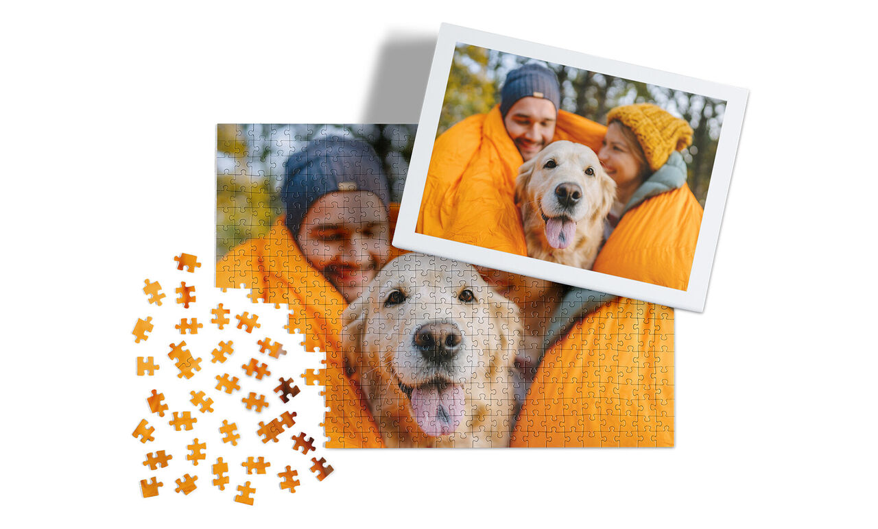 Two happy dogs in an orange blanket surrounded by puzzle pieces