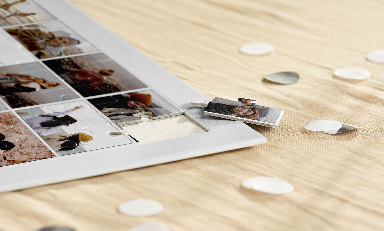 A creative photo collage in a white frame lies on elegant, light fabric. Small heart-shaped confetti surrounds the collage.