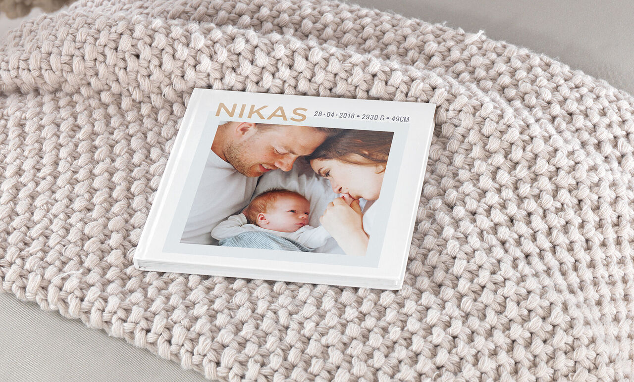 A CEWE PHOTO BOOK lies on a cozy blanket displaying a loving parent-child scene.