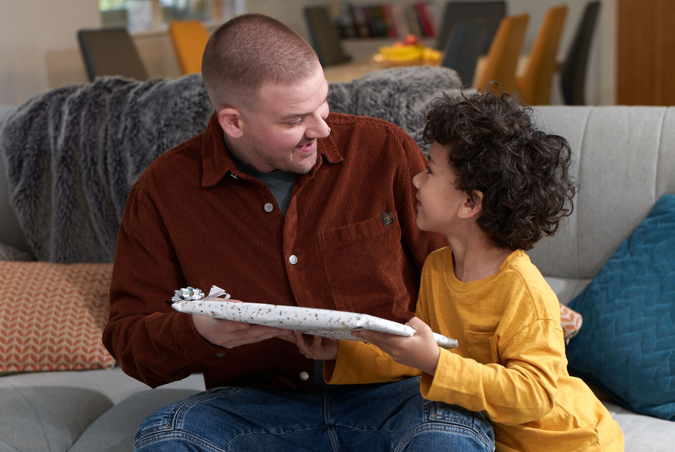 An adult and a child sitting on the sofa, with the child holding a gift.