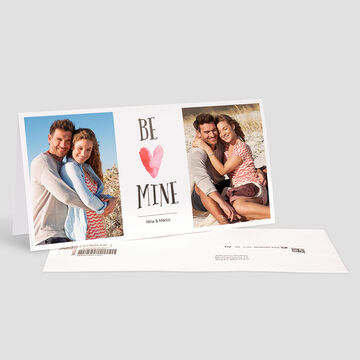 A joyful couple hugs at the beach. In between is a loving design with the words 'Be Mine'.
