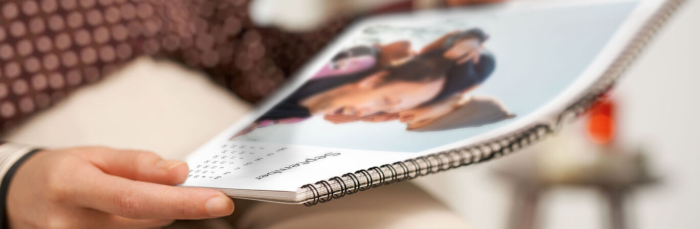 A person holding an open CEWE photo calendar with a picture of friends.
