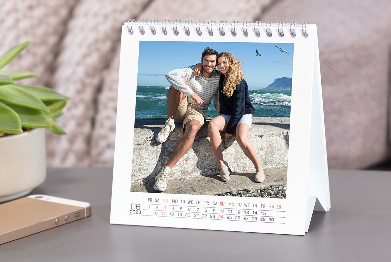 A couple cheerfully sitting on a wall overlooking the sea, surrounded by palm trees and sun.
