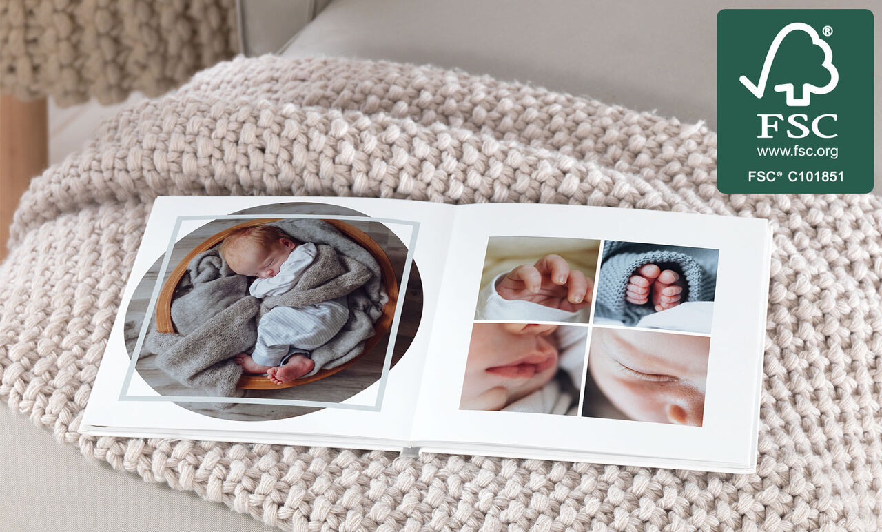 An open photo book with images of a sleeping baby and tiny feet, on a cozy knitted blanket. The book lies on a light table.