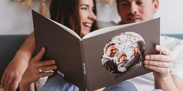 A couple sits comfortably on the sofa looking at a CEWE photo book with wonderful pictures