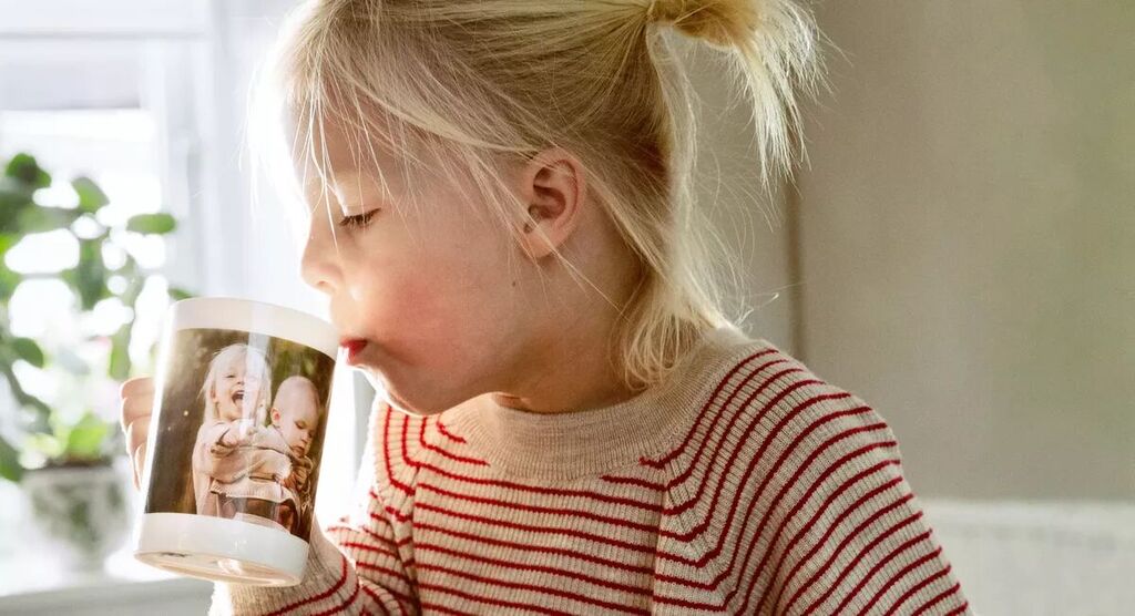 A child sits at the table with a cup in hand, featuring a photo, surrounded by plants.