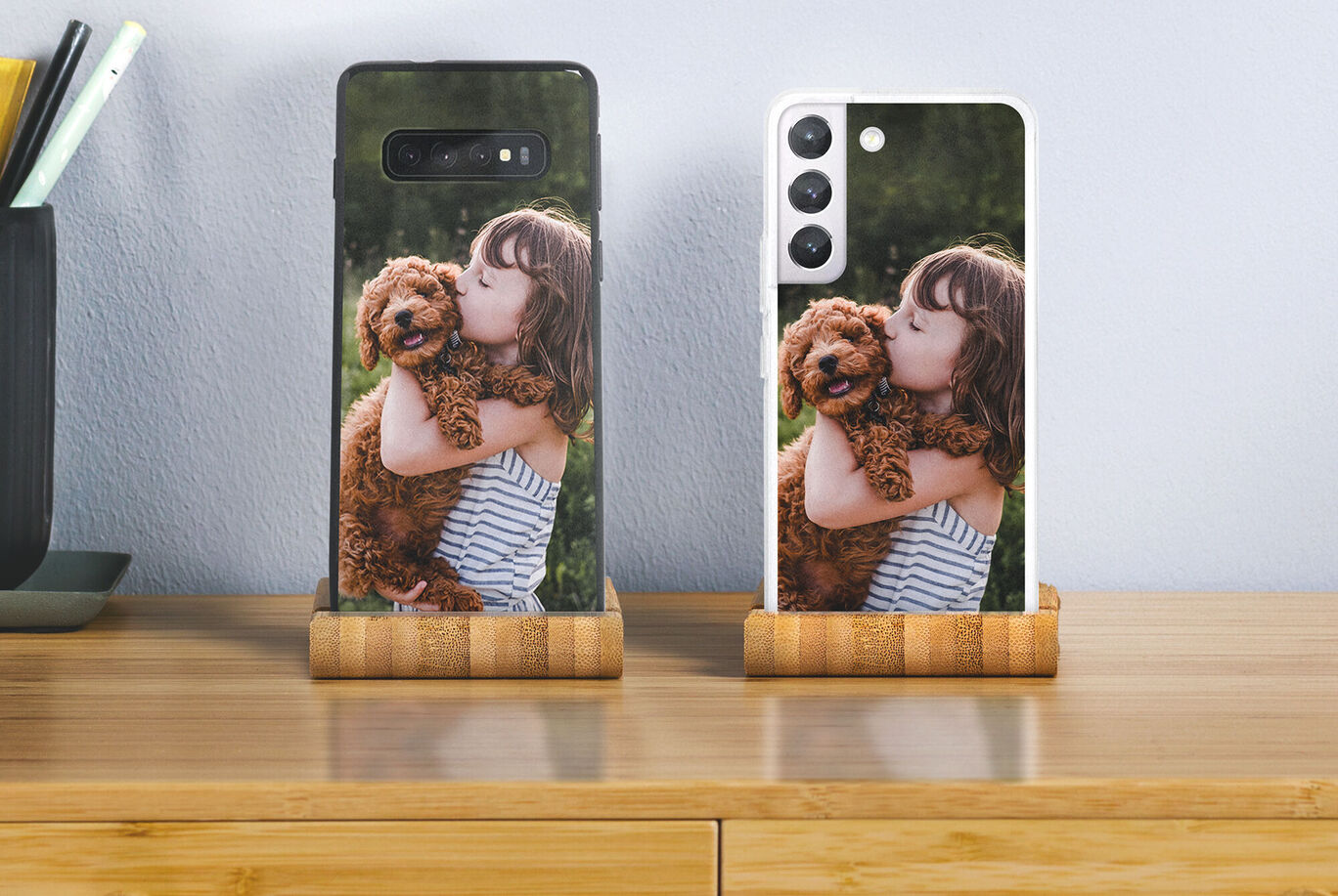 Two phones in a wooden holder, each showing a picture of a happy child and a dog together.