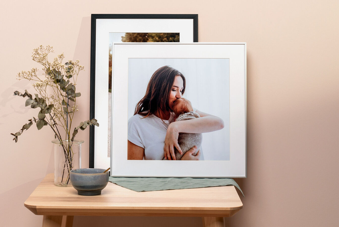Framed photo of a person with a pet on a wooden table, surrounded by a vase with flowers and a small dish.