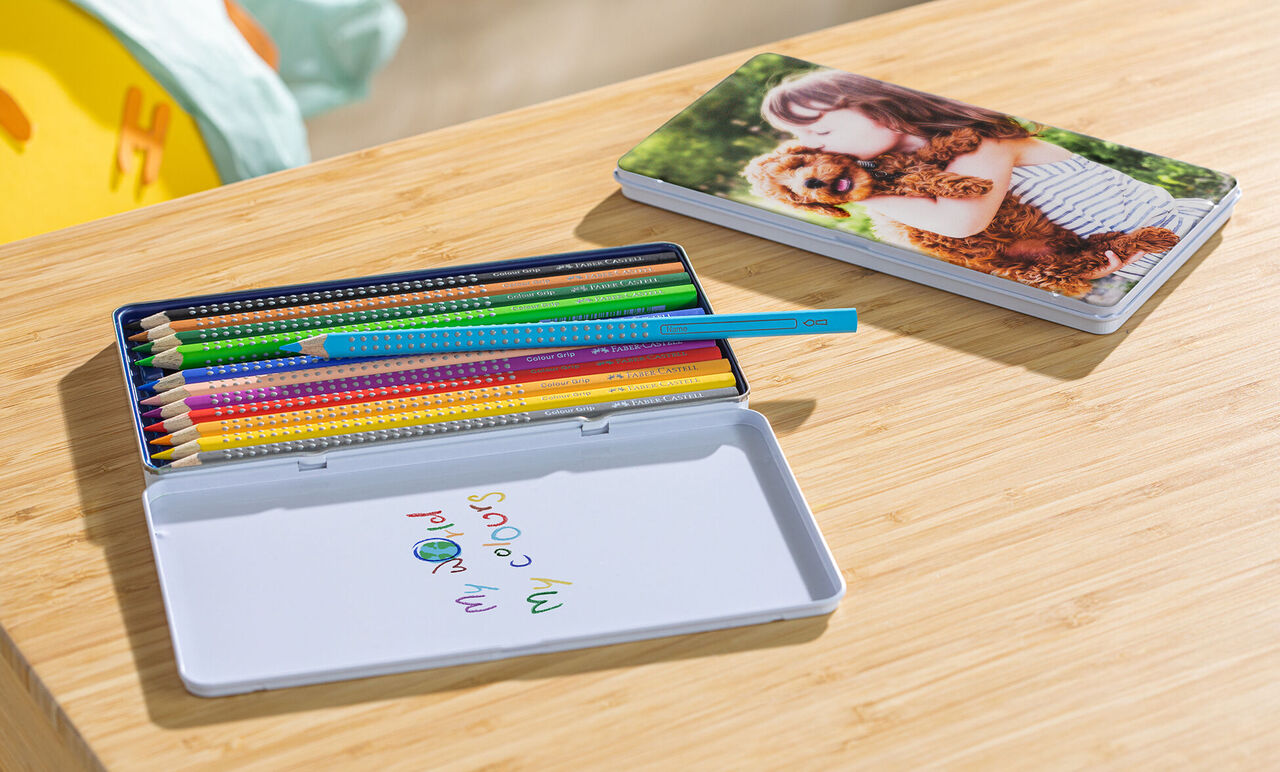 Colored pencils in a tin with a photo of a child and a dog in the background