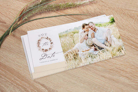 Couple sitting on a meadow holding an invitation, surrounded by natural elements.