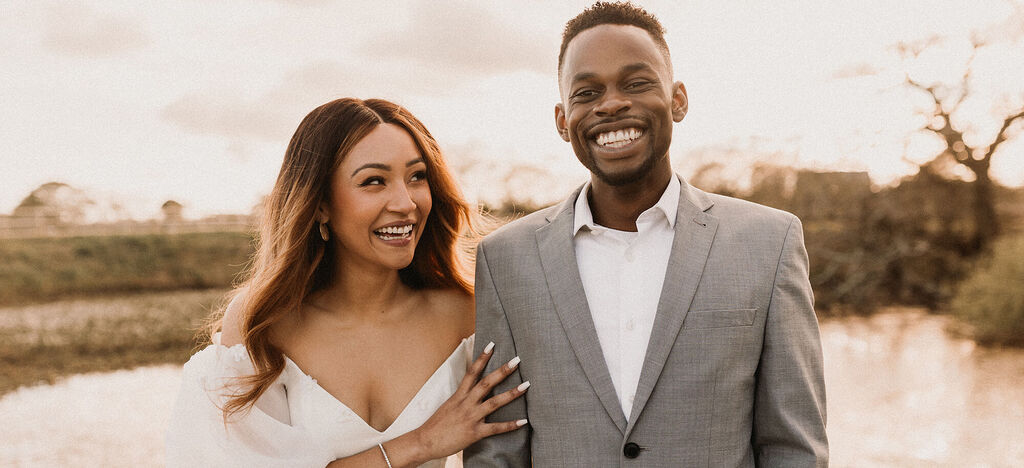 Happy couple posing by the water. The sunset creates a romantic ambiance.