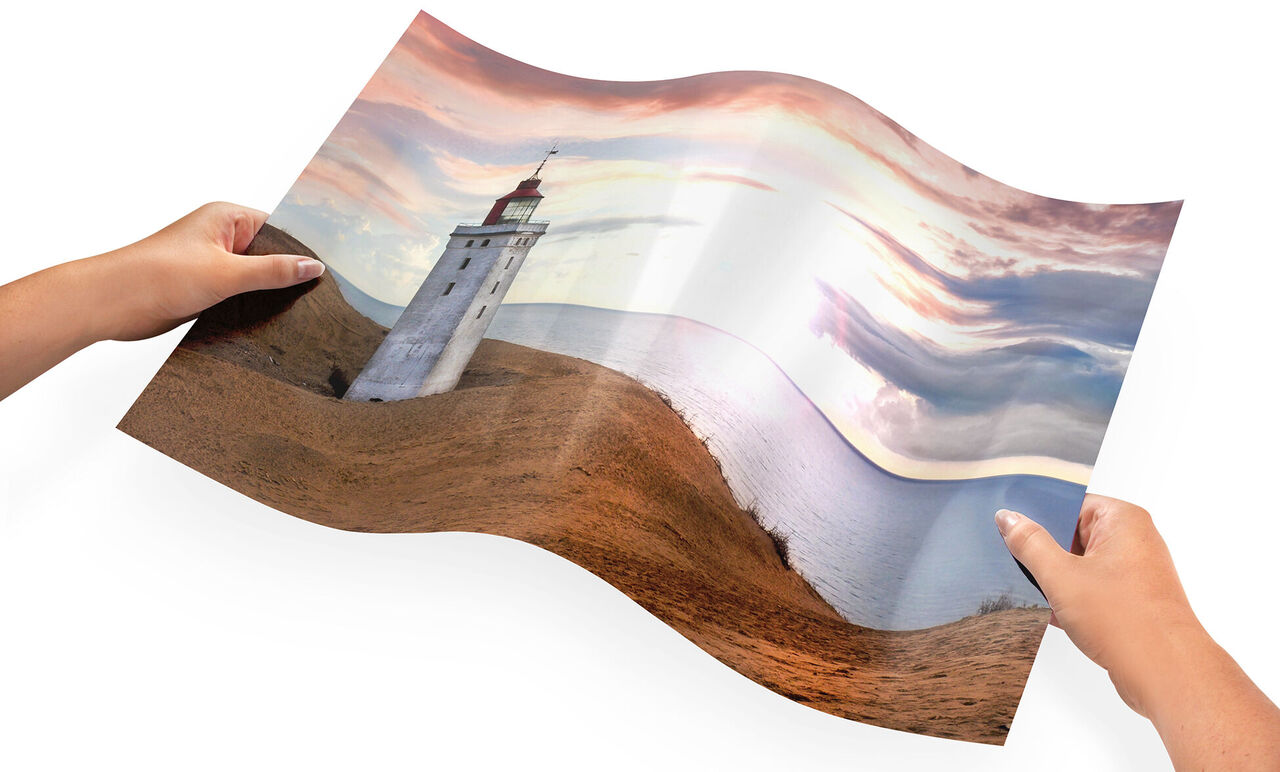 A person holding a curled photo poster of a lighthouse and a lake at sunset.