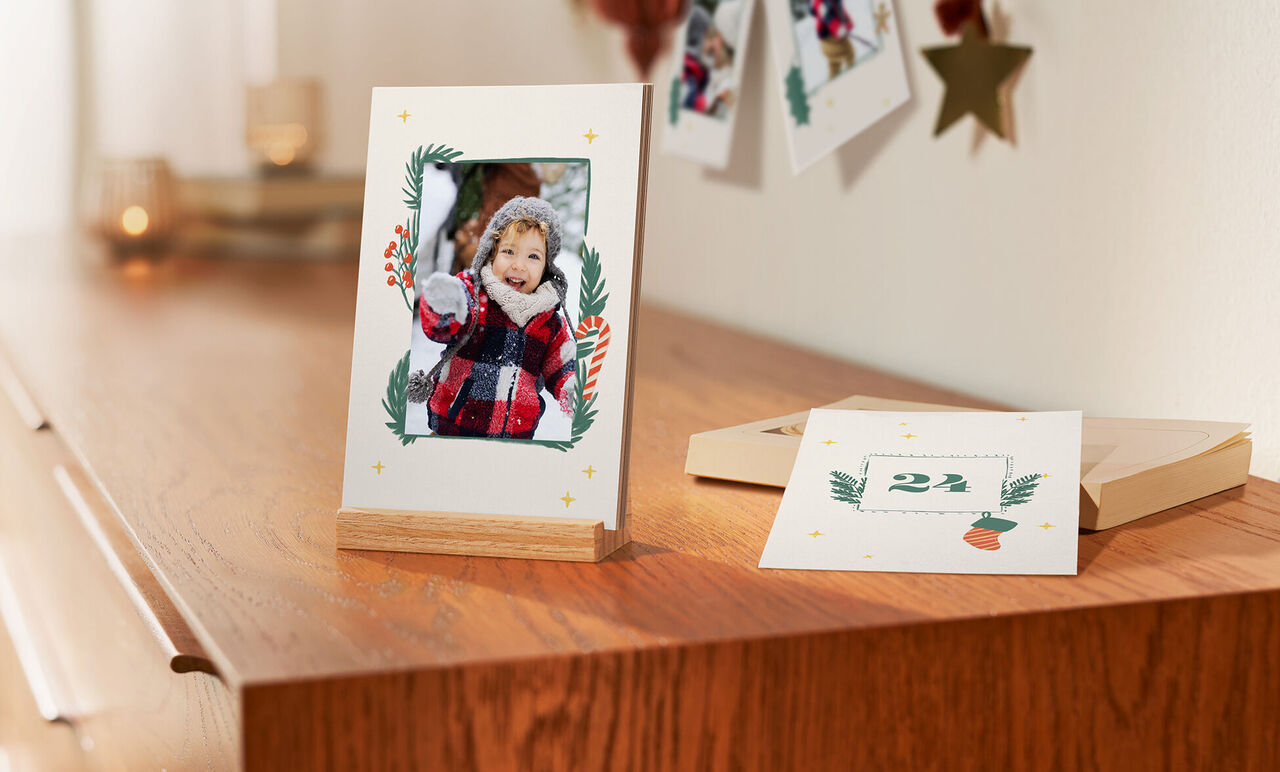 A framed photo sits on a wooden table. Next to it is a greeting card with festive design.