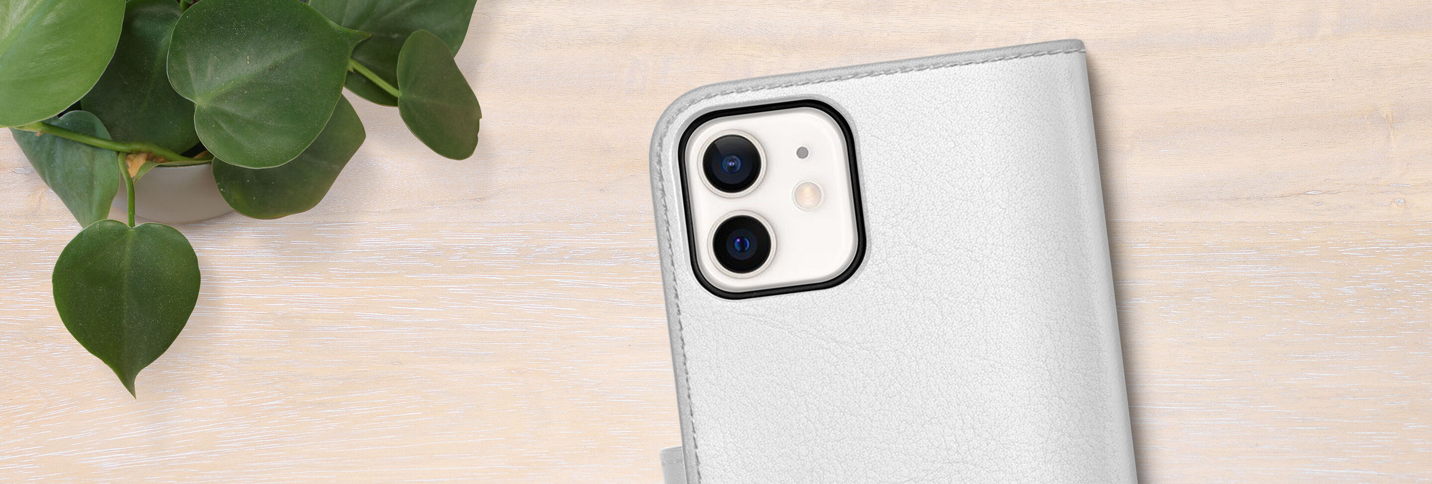 A white phone with case on a wooden table, surrounded by a green plant.