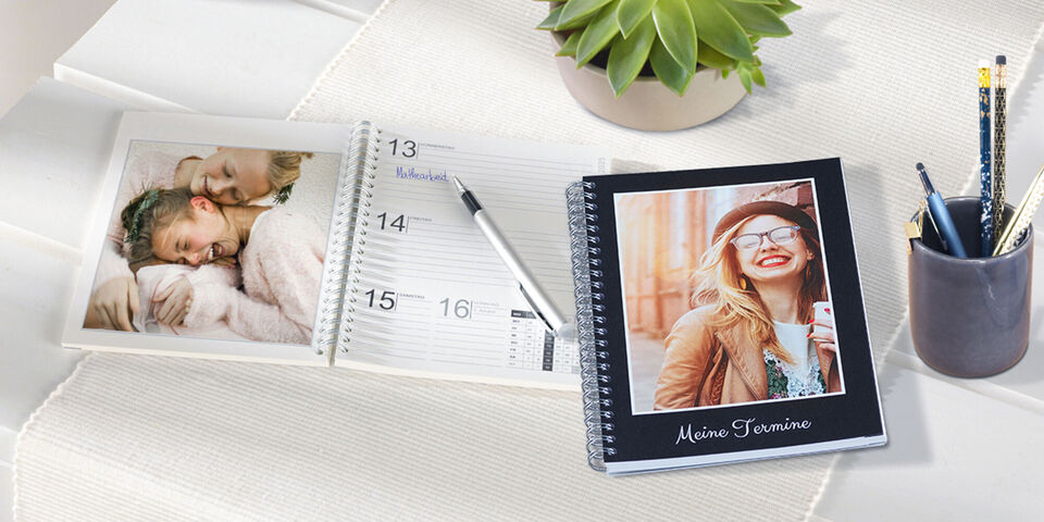 An individual photo calendar showcasing personal memories. In the foreground, an open calendar page with pictures, next to a pen holder with writing utensils.
