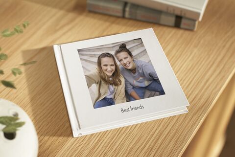 A photo book titled 'Best friends' on a wooden table, surrounded by a plant pot and books.
