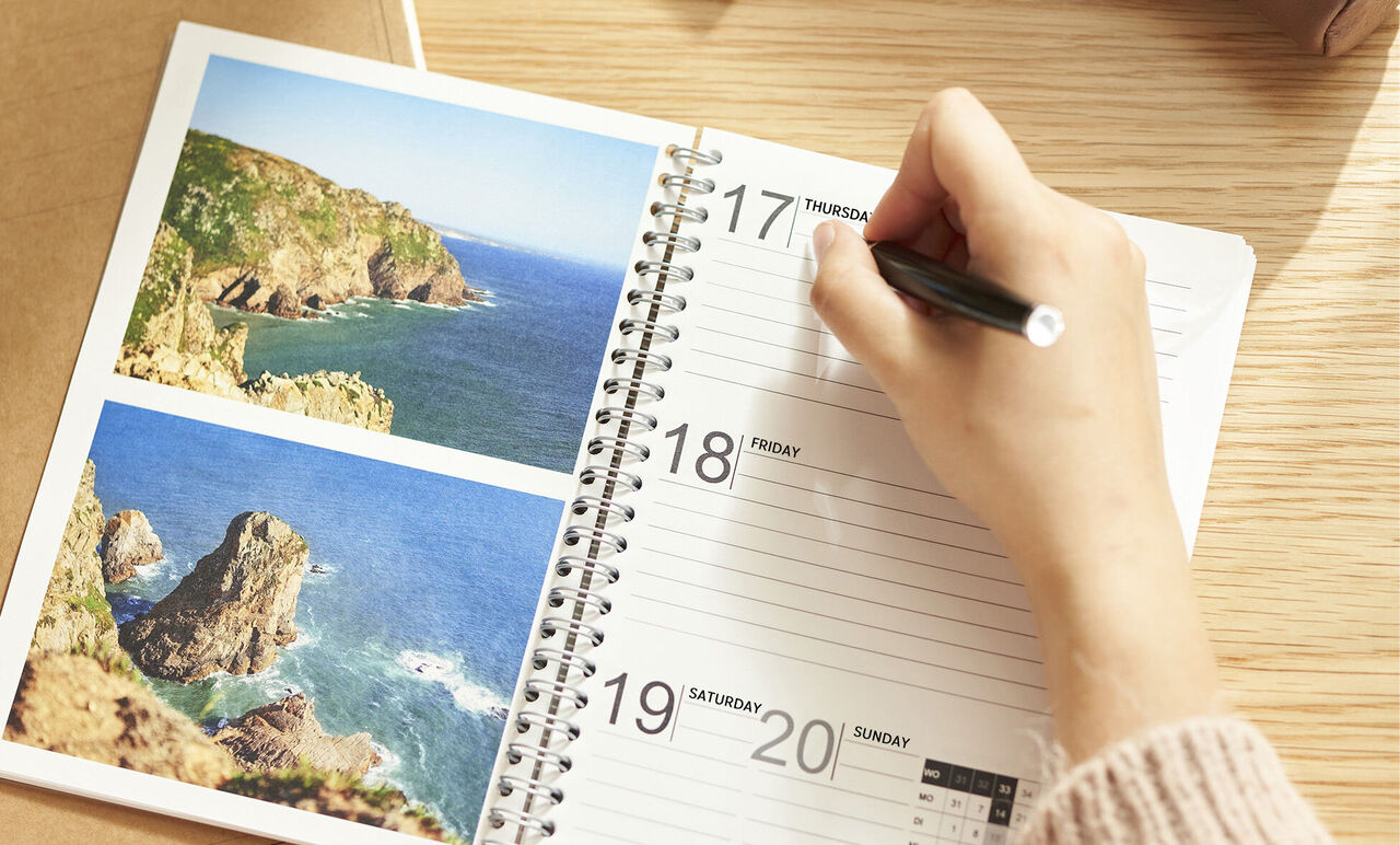A beautiful calendar with photos of coastal landscapes on the left side, while a hand writes an appointment.