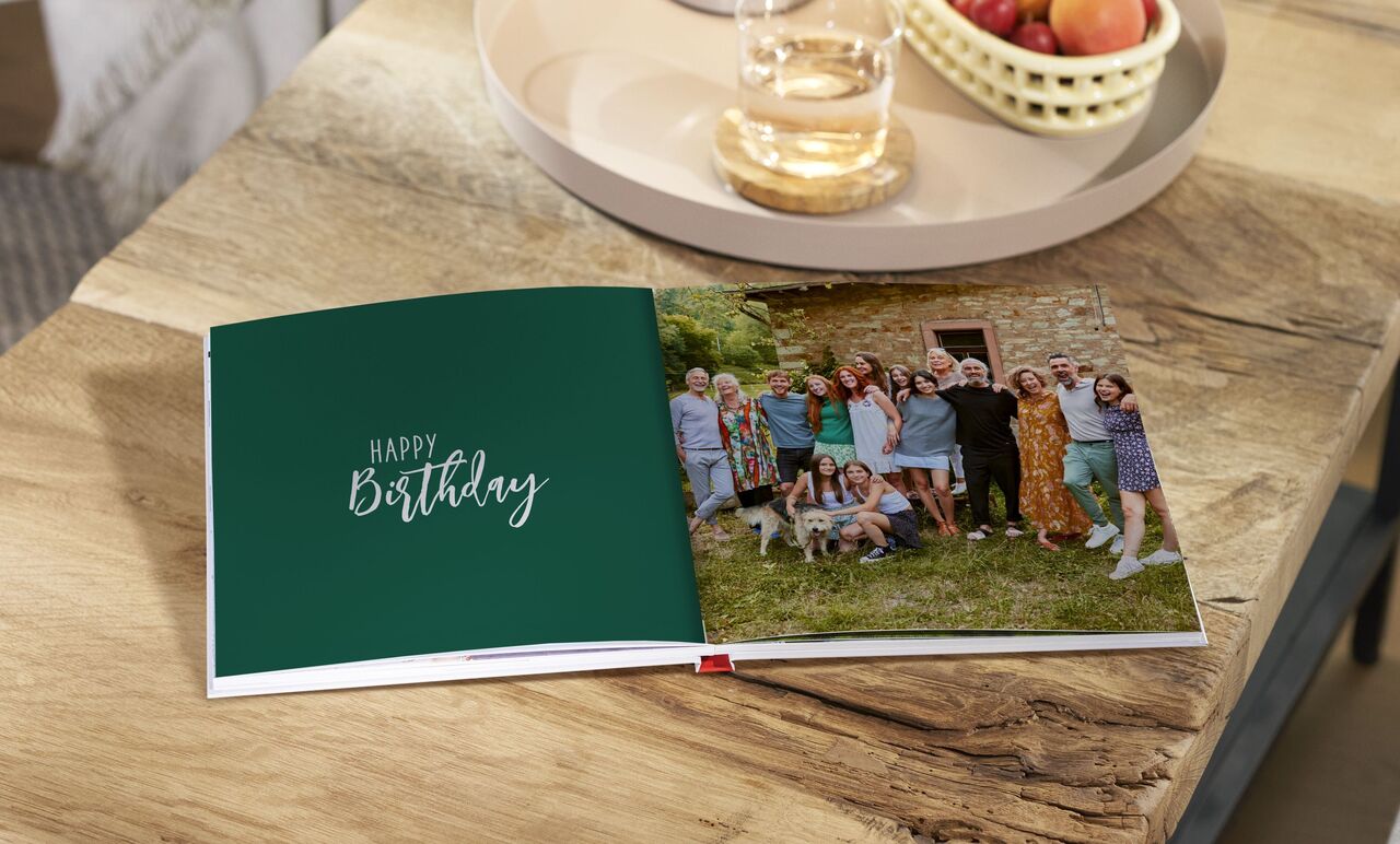 A group of people celebrating a birthday, surrounded by nature and a CEWE photo book on a table.
