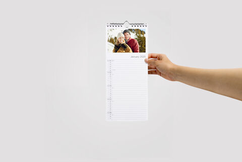 Hand holds a CEWE photo calendar with a joyful image and space for notes.