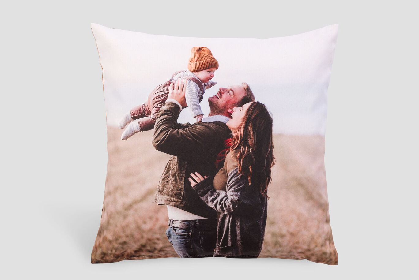 A cheerful family on a pillow. A father holds his baby in the air while the mother smiles warmly.