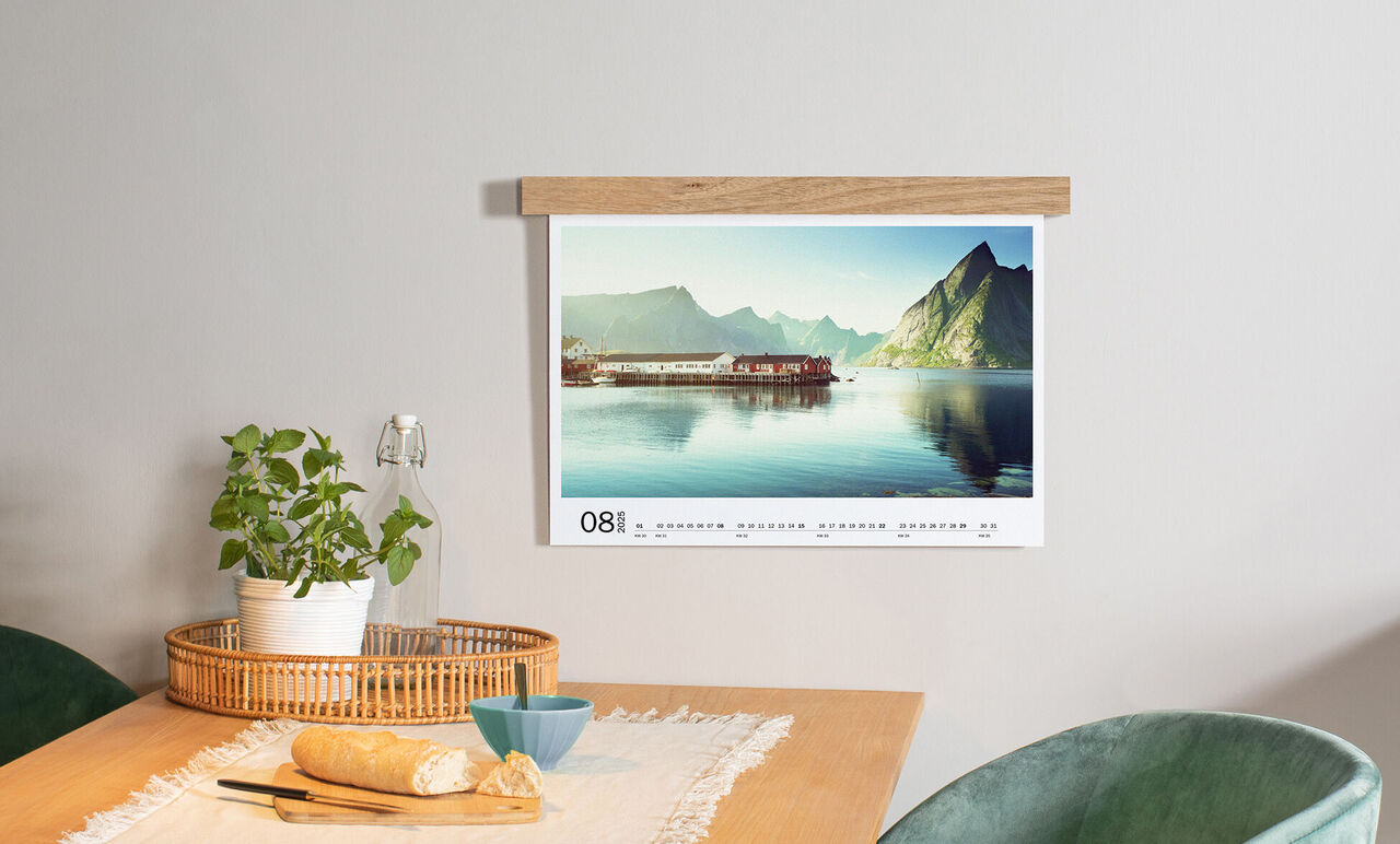 A modern designed calendar hanging on a wall above a table with a basket, dishes, and a plant.