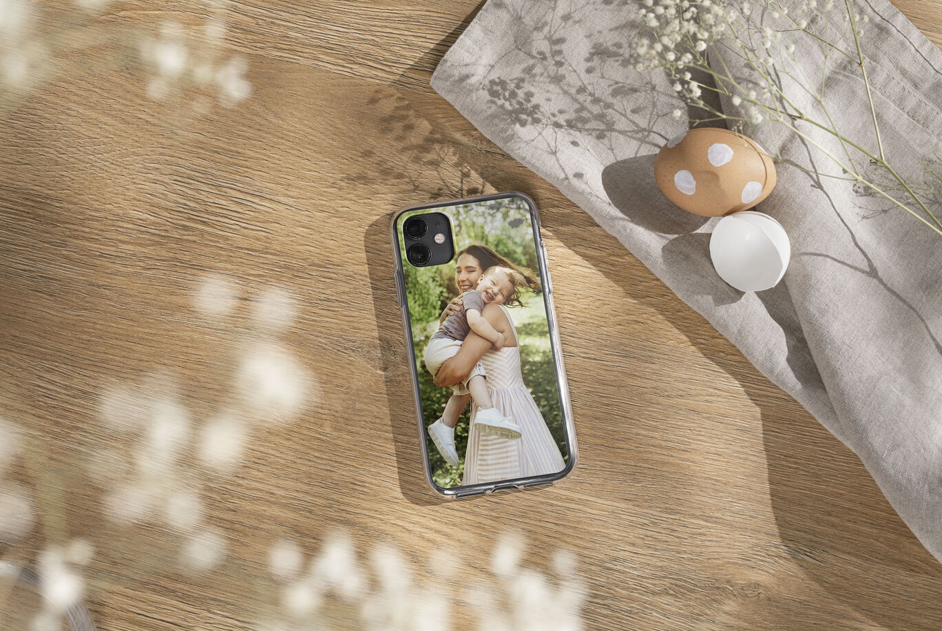 A phone showing a picture of a happy child sitting in a woman's arms, with soft flowers in the background.