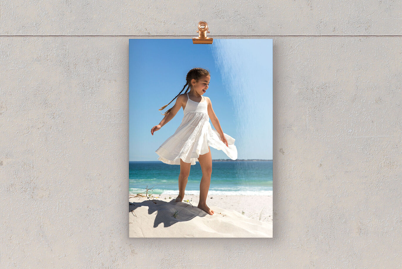 A girl in a white dress stands happily at the beach enjoying the sun.