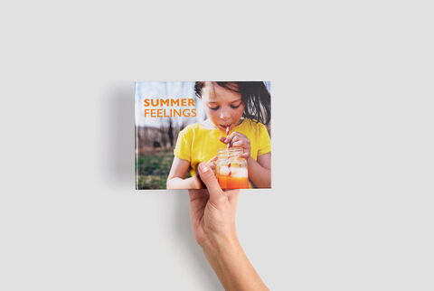 A hand holds a CEWE photo book titled "Summer Feelings".