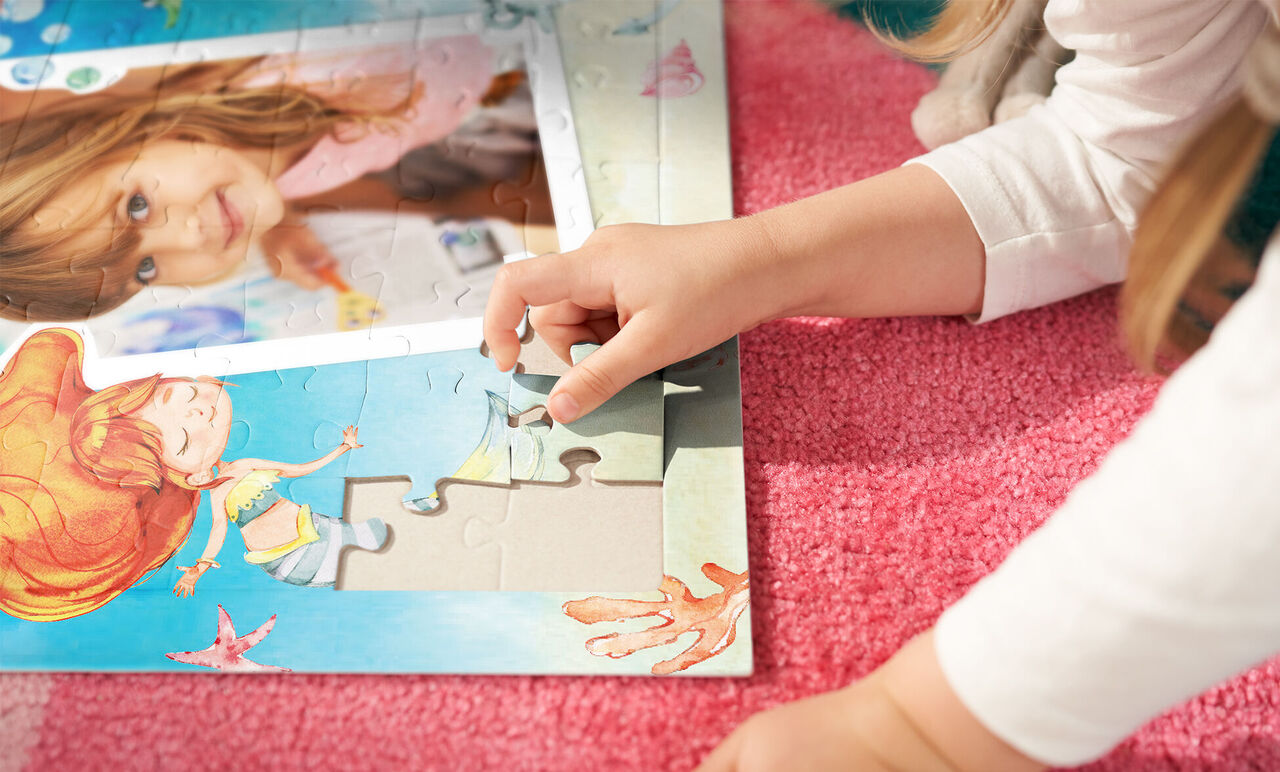 A child lies on a soft, pink carpet and adds a puzzle piece to a colorful puzzle. The puzzle shows cheerful sea creatures and a girl playing with them.
