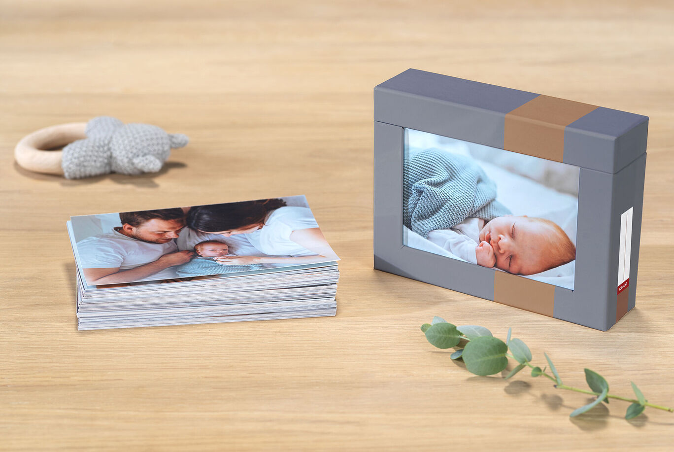 A lovingly designed photo book with baby pictures lies on a table, next to a stylish box with a baby picture and a wooden toy.