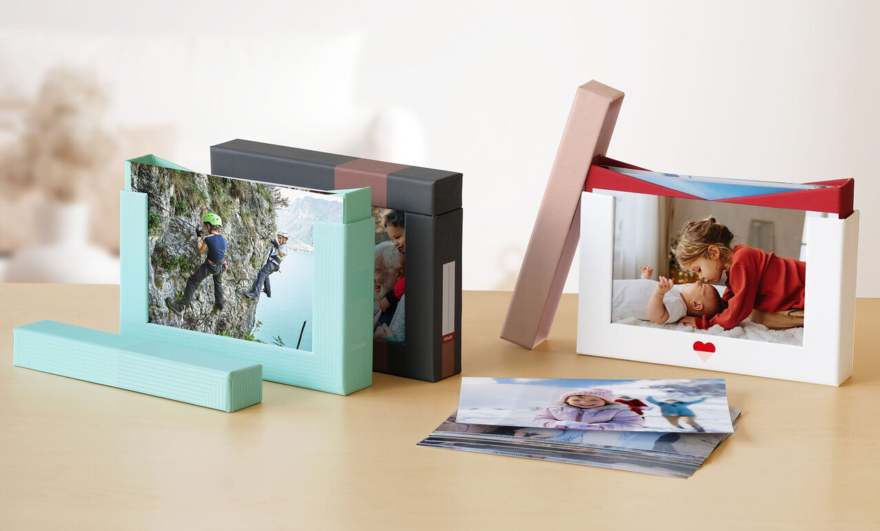 Two CEWE photo books on a table. One shows a child hugging a parent, and the other shows a mountain climber.