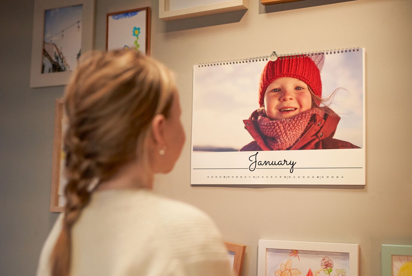 Woman looks at a wall calendar for January with a winter motif.