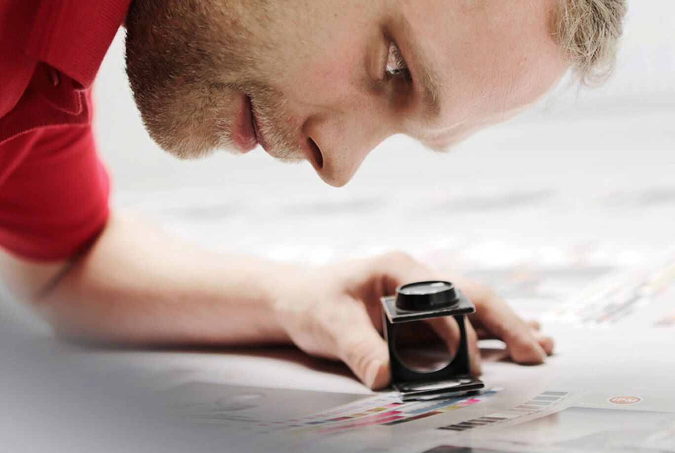 A person examines printed designs on a table with a magnifying glass.