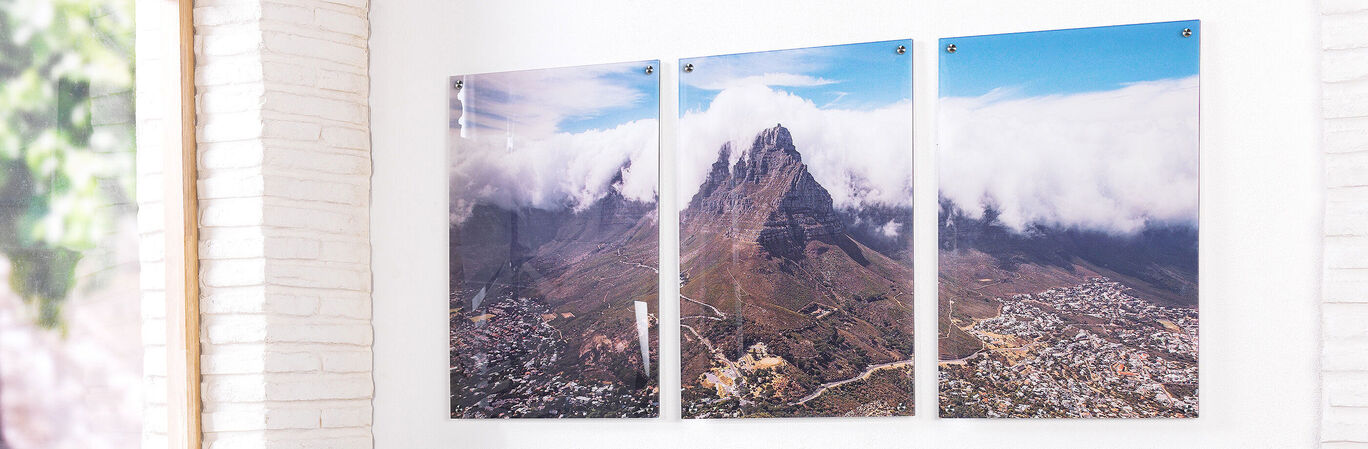 Three impressive art prints of a mountain with clouds hang on a white wall.