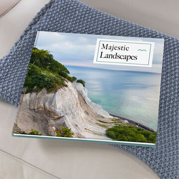 A beautiful photo book titled 'Majestic Landscapes' on a beige pillow, surrounded by a green landscape.