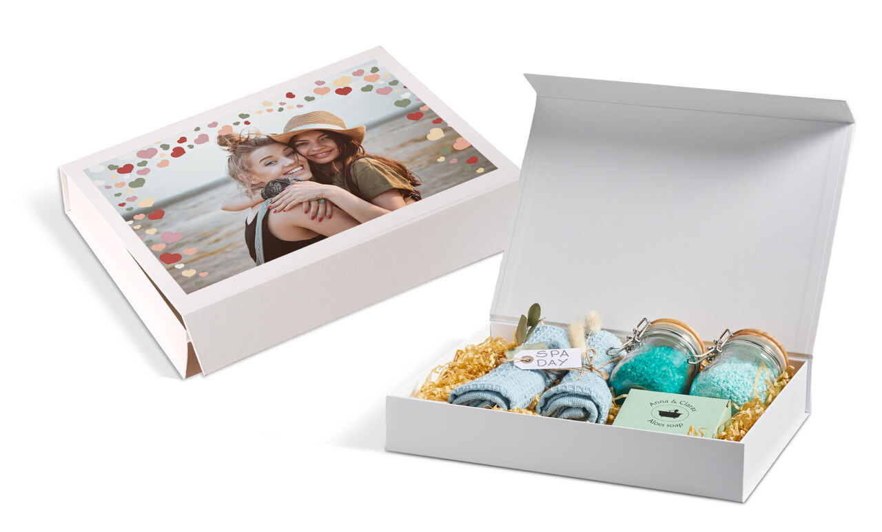 A creatively designed gift set with two happy women smiling at the camera. The gift box with content and a photo cover is in the foreground.