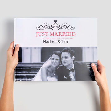 A happy couple holds their CEWE photo book "Just Married" in their hands. The book showcases their wedding moments.