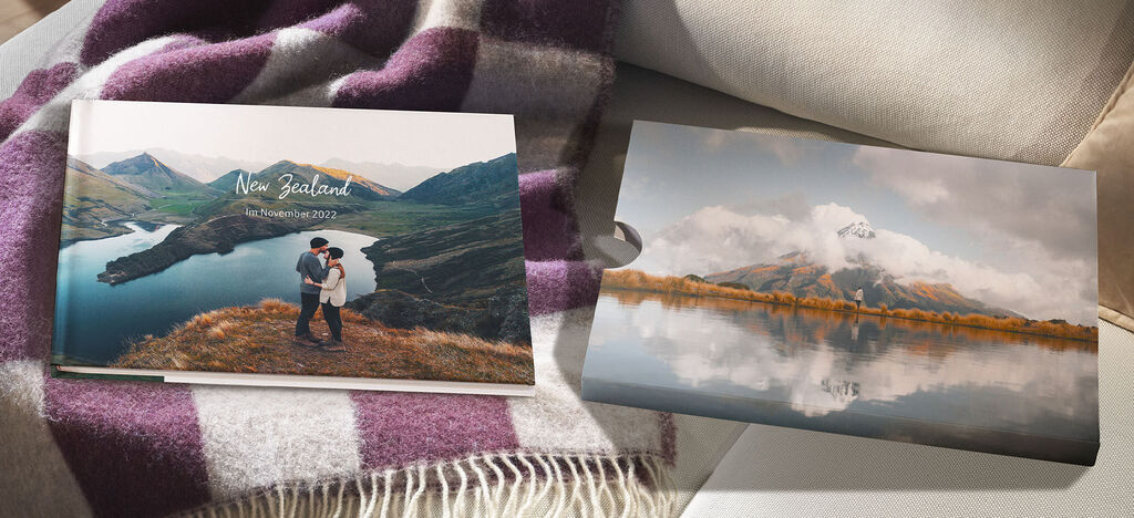 A couple stands in beautiful nature, embracing in front of a photo book titled 'New Zealand'. It reflects the peaceful landscape and their journey together.