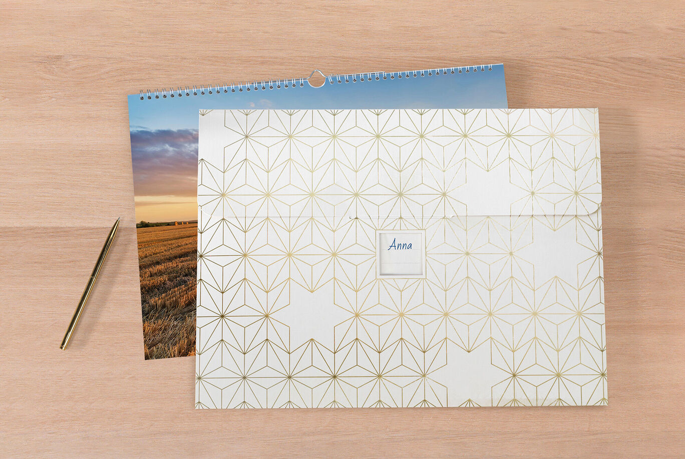 A lovingly designed CEWE photo calendar on a wooden table, next to a decorative envelope with the name 'Anna'.