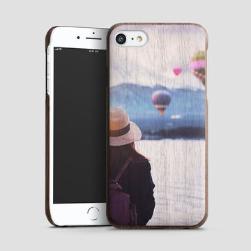 A woman with a hat stands in front of a phone. The display shows a beautiful background with hot air balloons.