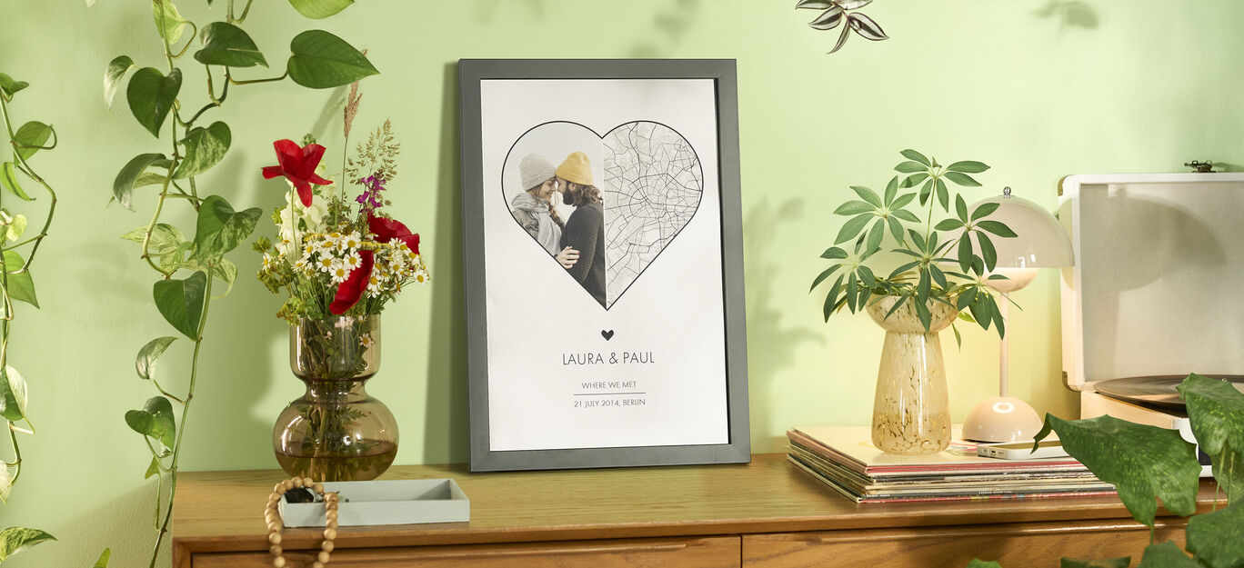 A framed picture with a heart design showing a couple embracing, surrounded by plants and a wooden shelf.