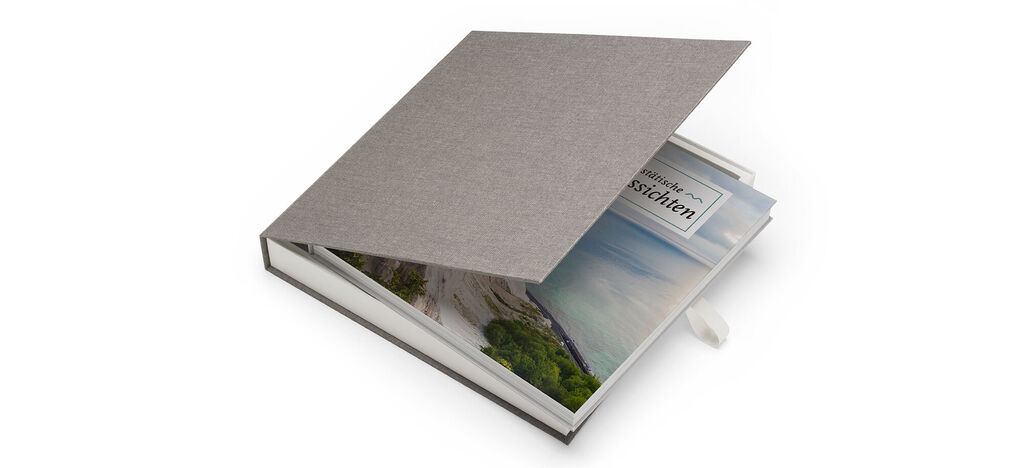 A lovingly designed CEWE PHOTOBOOK with a gray cover and open pages showing a vacation scene