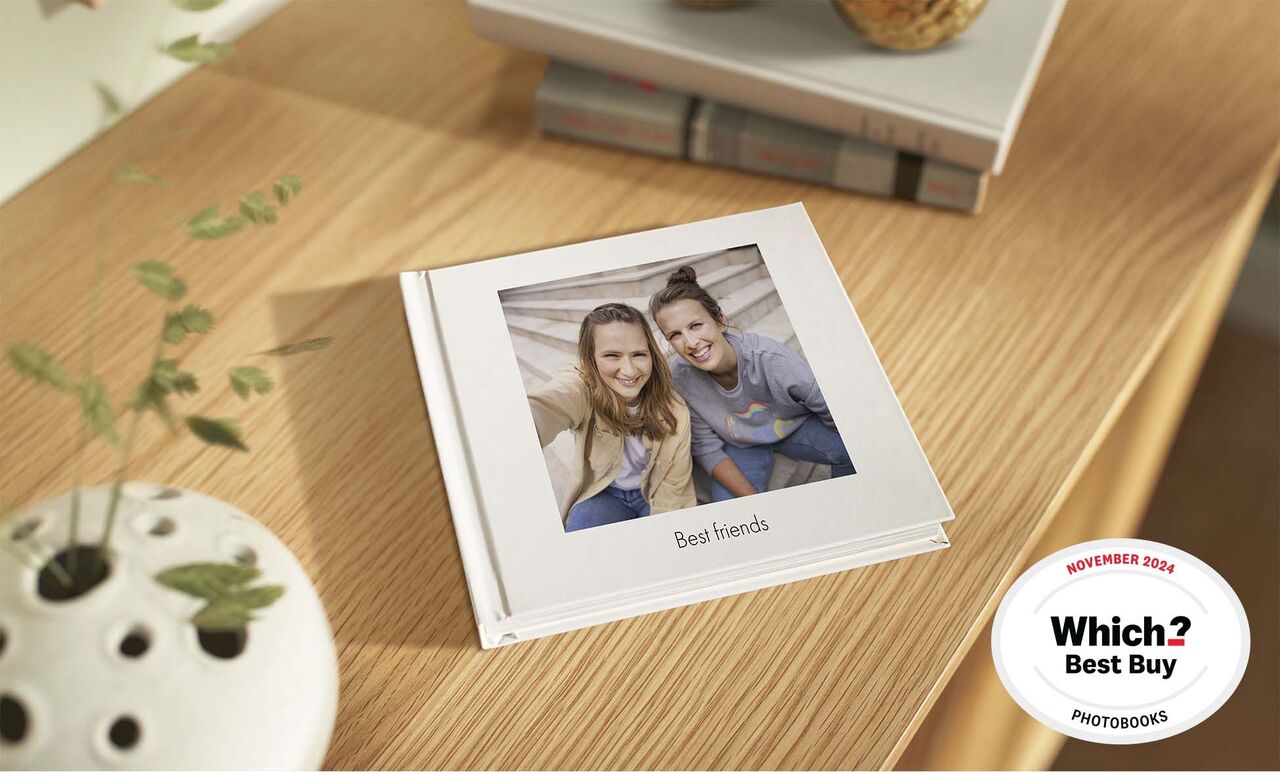 A stylish photo book titled "Best friends" on a bright wooden table, surrounded by a houseplant and books.