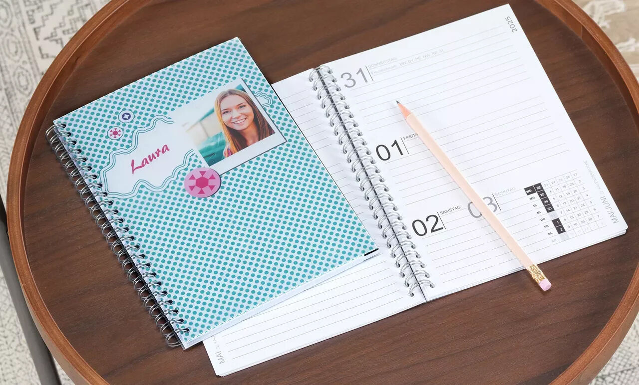 A lovingly designed notebook on a table, decorated with a photo and colorful elements. A blank calendar lies beside it.